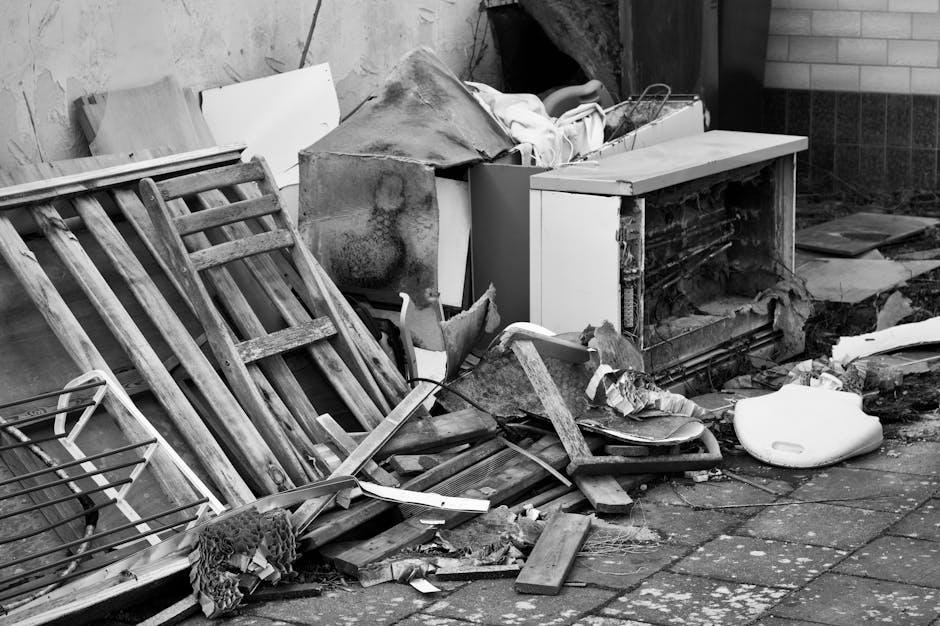 A pile of discarded household waste and broken furniture on an outdoor paved area. The debris includes wooden slats from a dismantled bed frame, with a weathered, aged texture and visible grain, leani